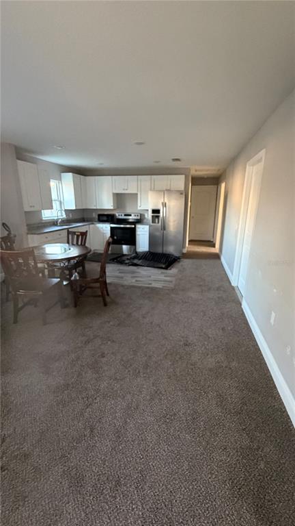 An open-concept kitchen and dining area features white cabinets, stainless steel appliances, and carpeted flooring — 2117 WINGER AVENUE, HAINES CITY, FL