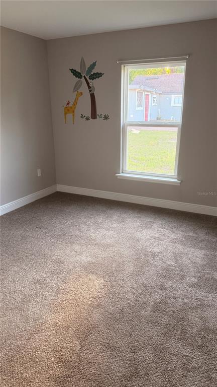 An empty bedroom features beige carpet, light gray walls, a window, and a giraffe wall decal — 2117 WINGER AVENUE, HAINES CITY, FL