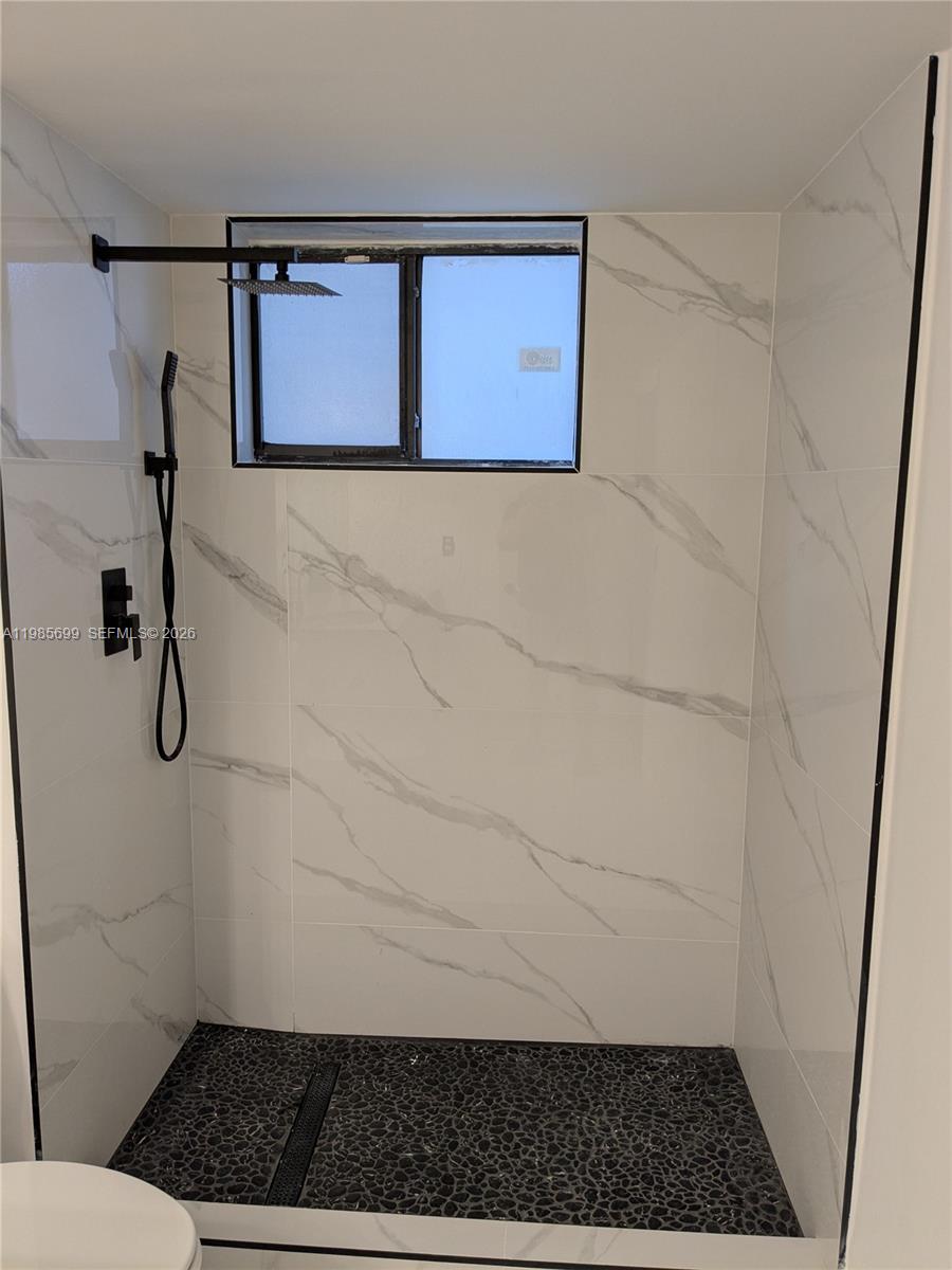 A walk-in shower features white marble-look wall tiles, a black pebble floor, and black fixtures — 601 Ives Dairy Rd # 8, Miami FL 33179, MIAMI, FL