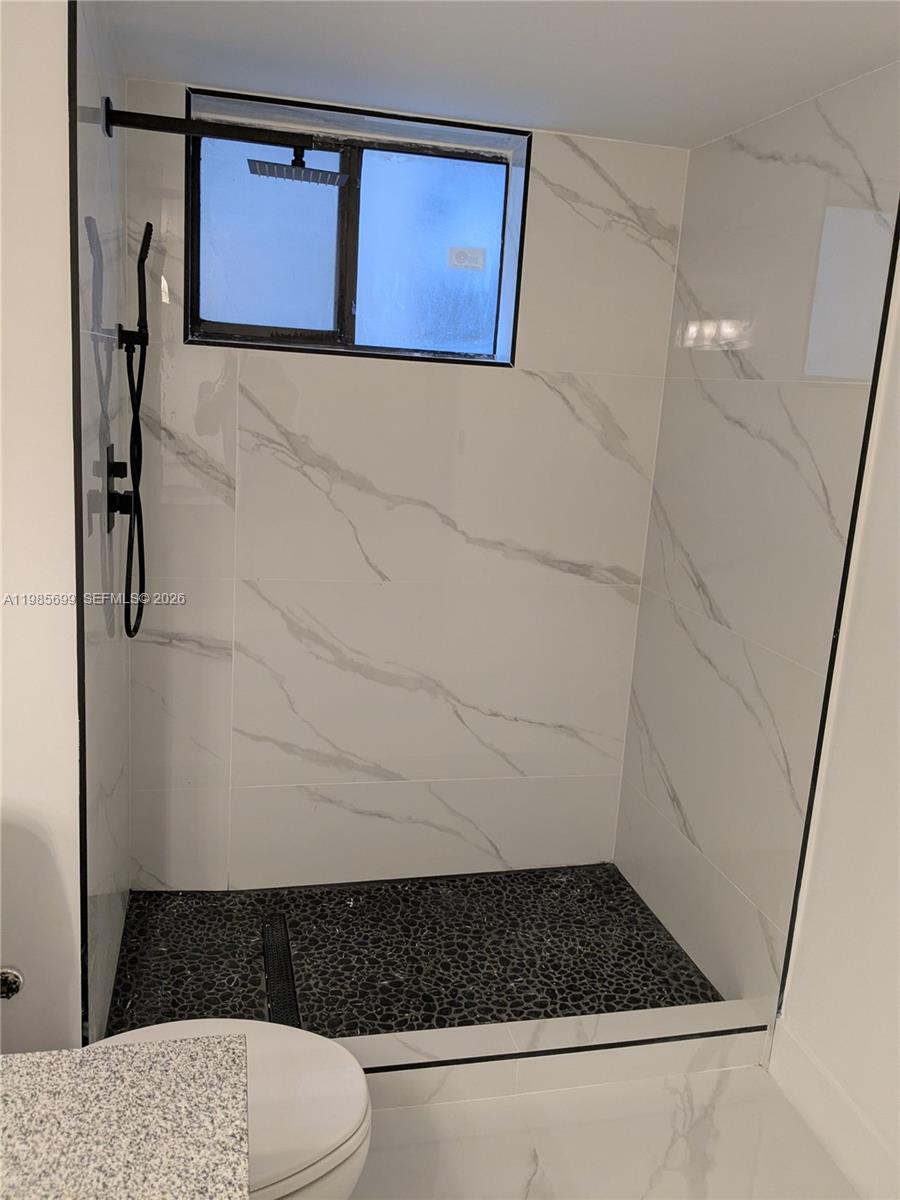 A walk-in shower features white marble-look wall tiles, a black pebble floor, and black fixtures — 601 Ives Dairy Rd # 8, Miami FL 33179, MIAMI, FL