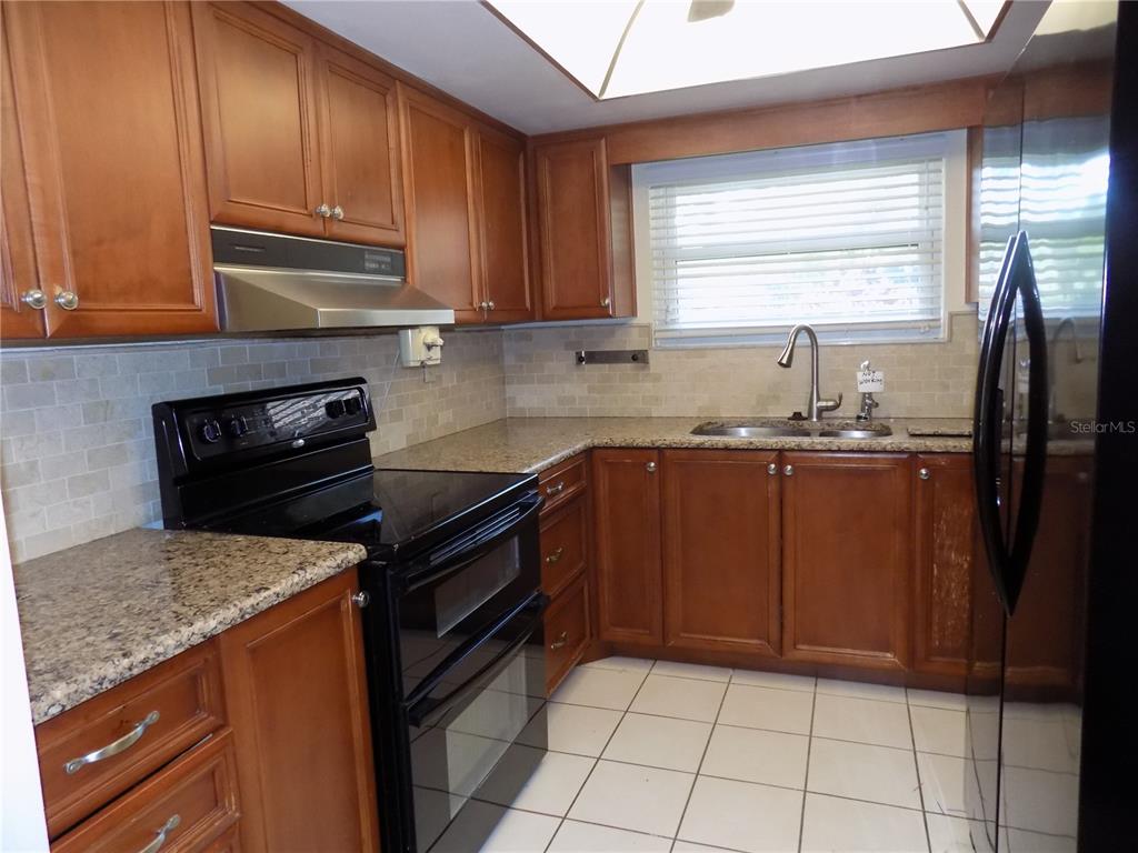 A kitchen features wood cabinets, granite countertops, a black stove, and a tiled floor — 9663 86TH AVENUE UNIT 9663, SEMINOLE, FL