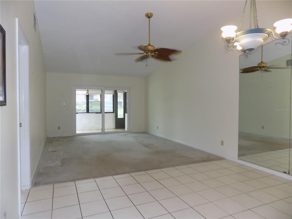 A living room with a vaulted ceiling, ceiling fan, carpeted floor, and a mirrored wall — 9663 86TH AVENUE UNIT 9663, SEMINOLE, FL