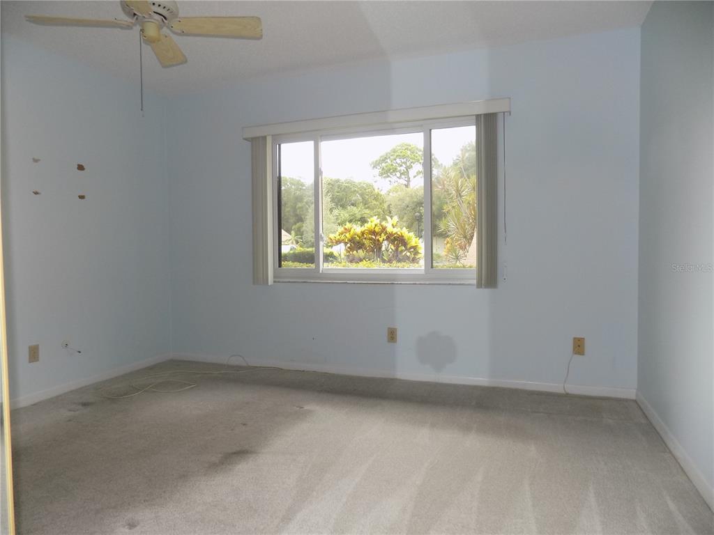 An empty bedroom with light blue walls, beige carpeting, a ceiling fan, and a large window — 9663 86TH AVENUE UNIT 9663, SEMINOLE, FL