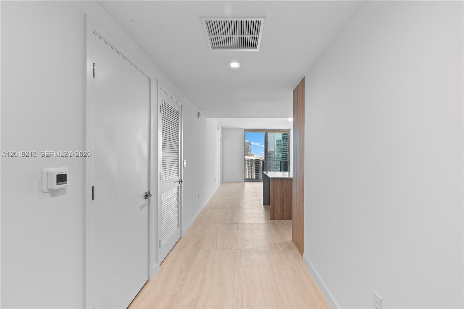 A hallway with light tile flooring leads toward a kitchen and a balcony view — 77 SE 5 # 3702, Miami FL 33131, MIAMI, FL