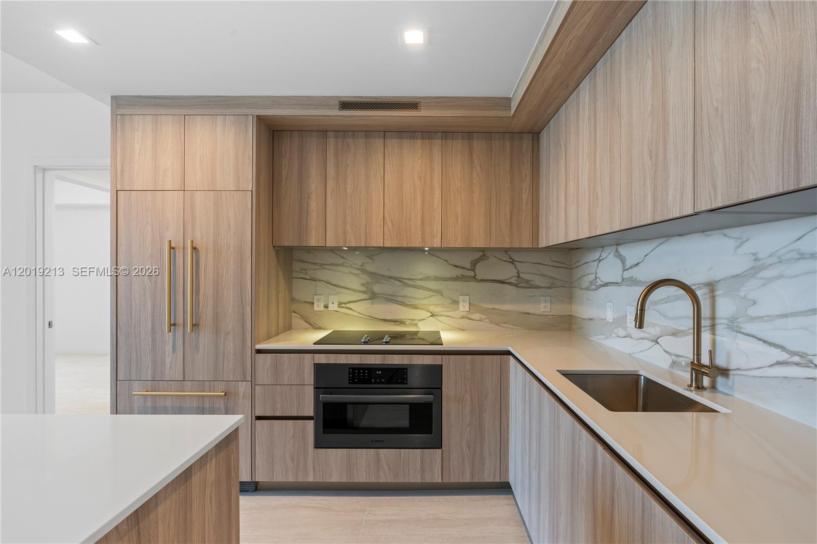 A modern kitchen features light wood cabinetry, marble-patterned backsplashes, and a stainless steel sink — 77 SE 5 # 3702, Miami FL 33131, MIAMI, FL