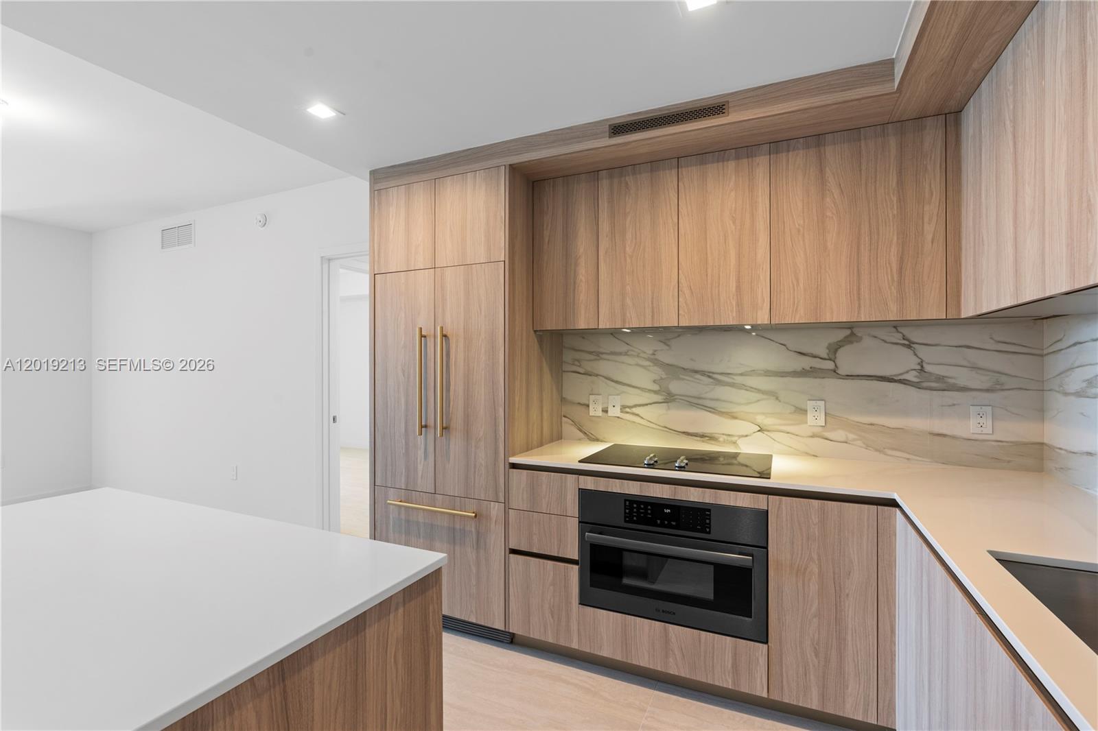 A modern kitchen features wood-grain cabinetry, a marble backsplash, and integrated stainless steel appliances — 77 SE 5 # 3702, Miami FL 33131, MIAMI, FL