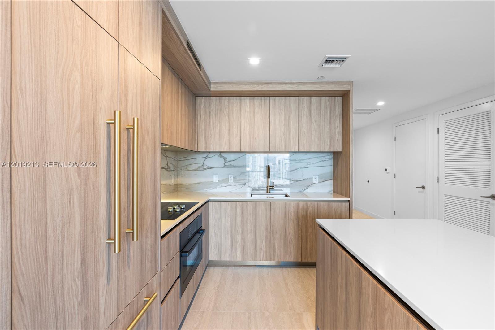 A modern kitchen features light wood cabinetry, a white countertop, and a marble backsplash — 77 SE 5 # 3702, Miami FL 33131, MIAMI, FL