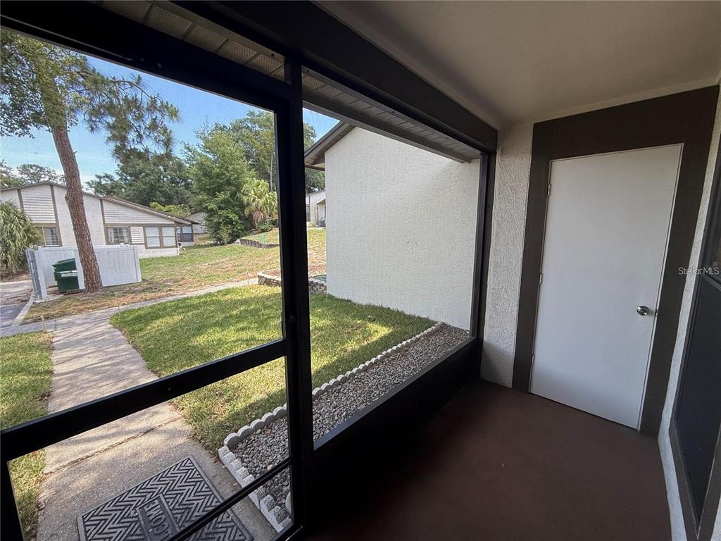 A screened-in porch features a concrete floor, a white door, and views of a lawn — 2130 BANCROFT PLACE UNIT B, PALM HARBOR, FL