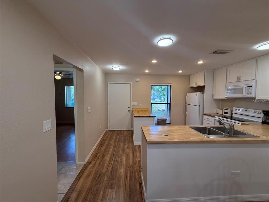 A kitchen with light-colored cabinets, wood countertops, and wood-look flooring opens to a hallway — 2130 BANCROFT PLACE UNIT B, PALM HARBOR, FL