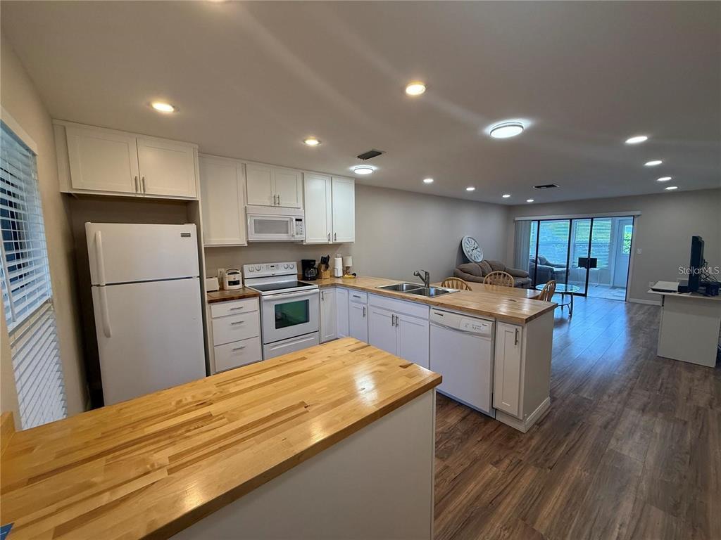 A kitchen with white cabinets, butcher block countertops, and stainless steel appliances opens to a living area — 2130 BANCROFT PLACE UNIT B, PALM HARBOR, FL