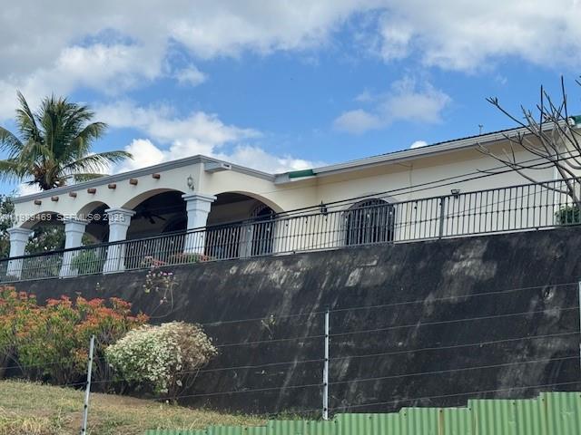 A light-colored house with a covered porch sits atop a tall, dark retaining wall — KM 9.5 Carretera Vieja A. Leon, NI Man, NI