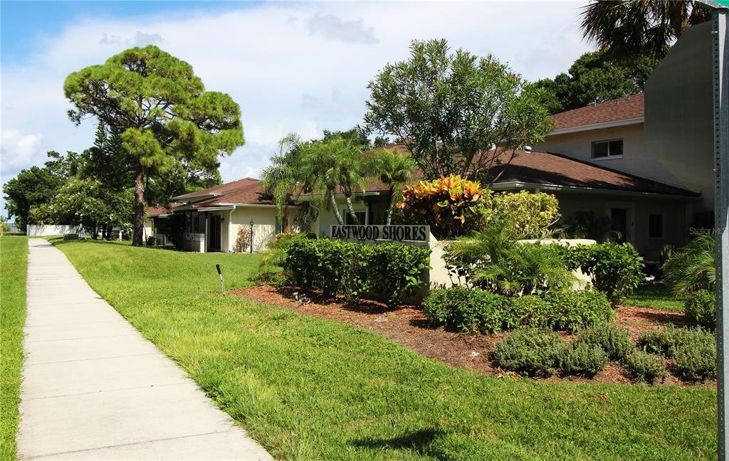 A sidewalk leads past a landscaped sign for Eastwood Shores toward residential buildings and trees — 1829 BOUGH AVENUE UNIT 4, CLEARWATER, FL