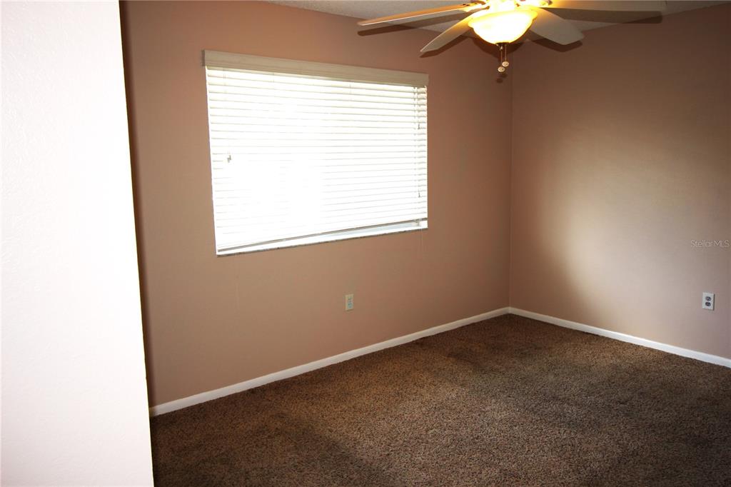 An empty bedroom features tan walls, brown carpeting, a ceiling fan, and a window with blinds — 1829 BOUGH AVENUE UNIT 4, CLEARWATER, FL