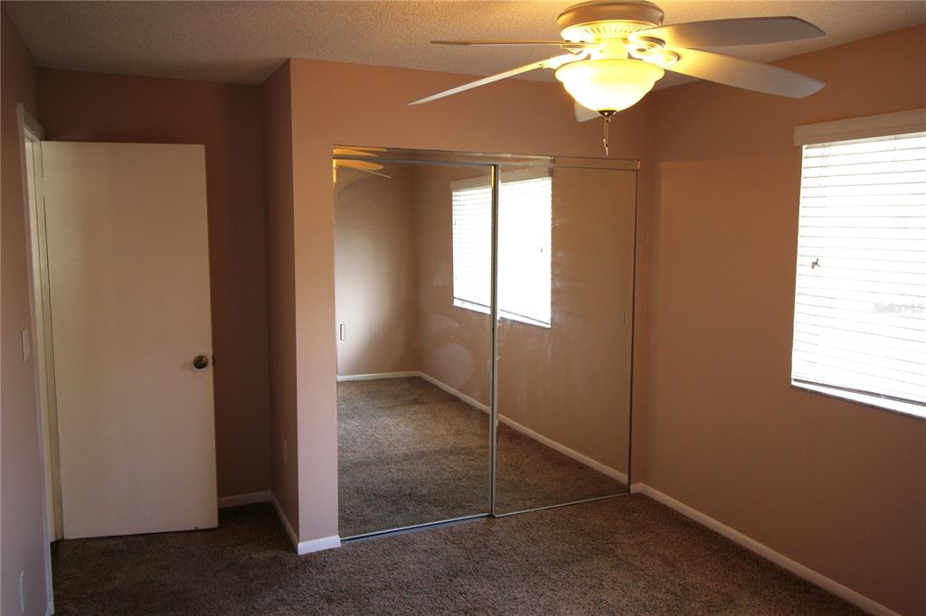 A bedroom features tan walls, brown carpeting, a ceiling fan, and mirrored sliding closet doors — 1829 BOUGH AVENUE UNIT 4, CLEARWATER, FL