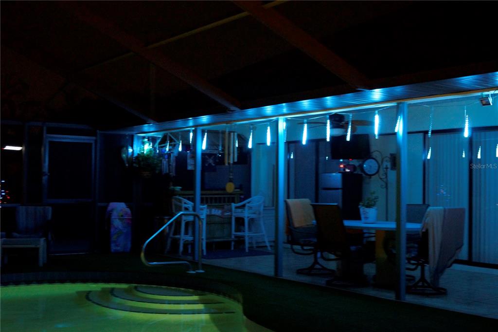 A covered outdoor patio with a swimming pool, bar area, and blue string lighting at night — 120 CUIABA DRIVE, PUNTA GORDA, FL
