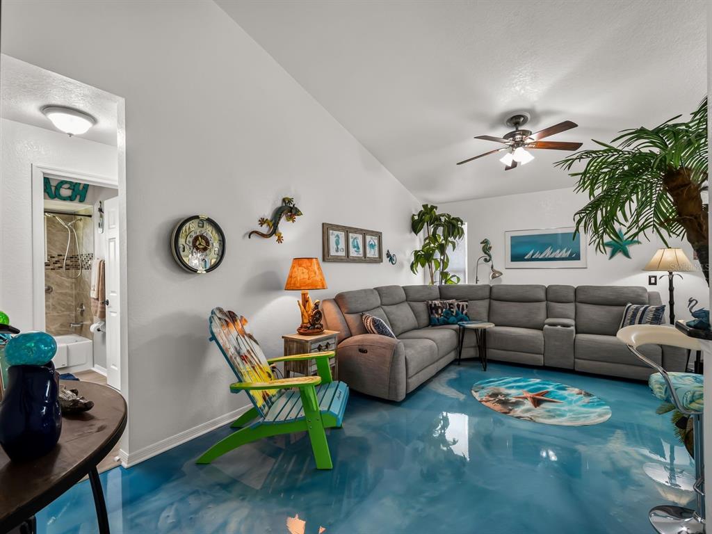 A living room features a blue epoxy floor, a gray sectional sofa, and beach-themed decor — 120 CUIABA DRIVE, PUNTA GORDA, FL