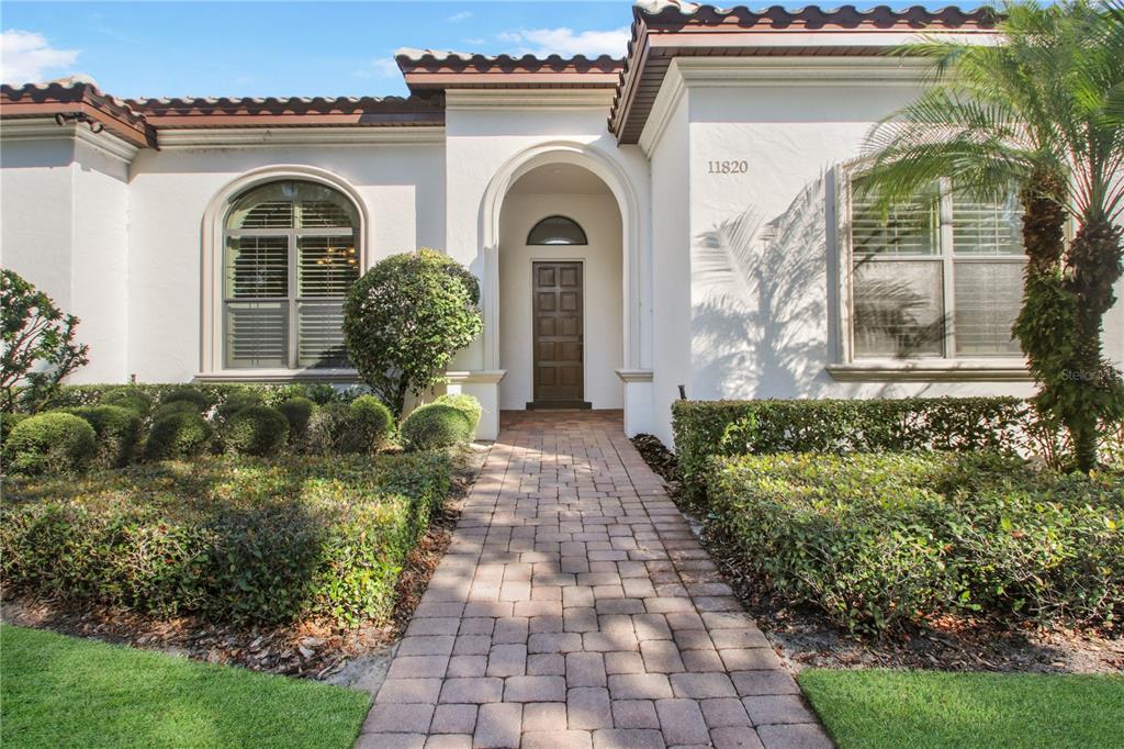 A white stucco house features a brown front door, arched entryway, and a paved walkway — 11820 WATERSTONE LOOP DRIVE, WINDERMERE, FL