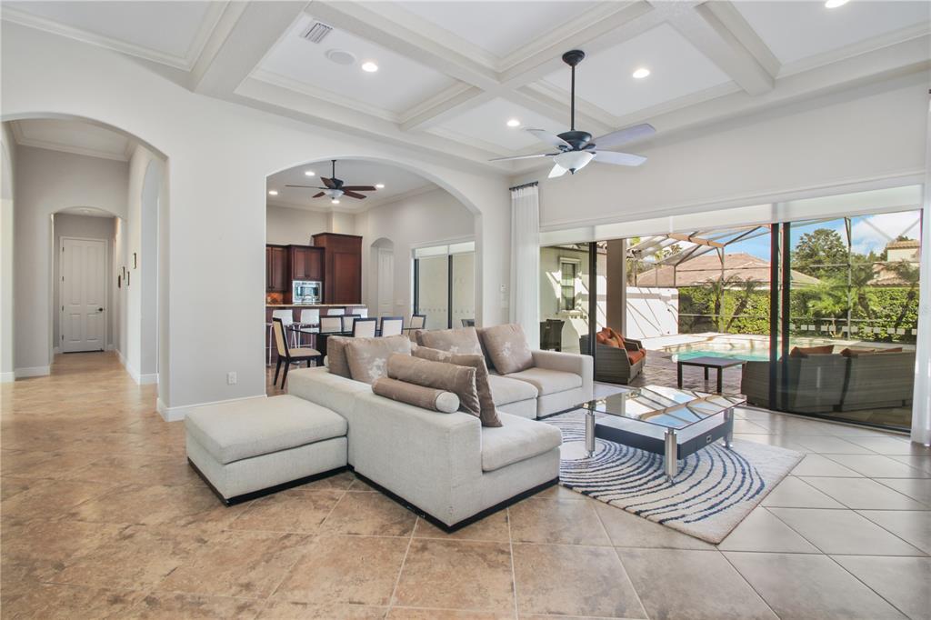 A living room with a coffered ceiling and tile floors opens to a pool patio — 11820 WATERSTONE LOOP DRIVE, WINDERMERE, FL