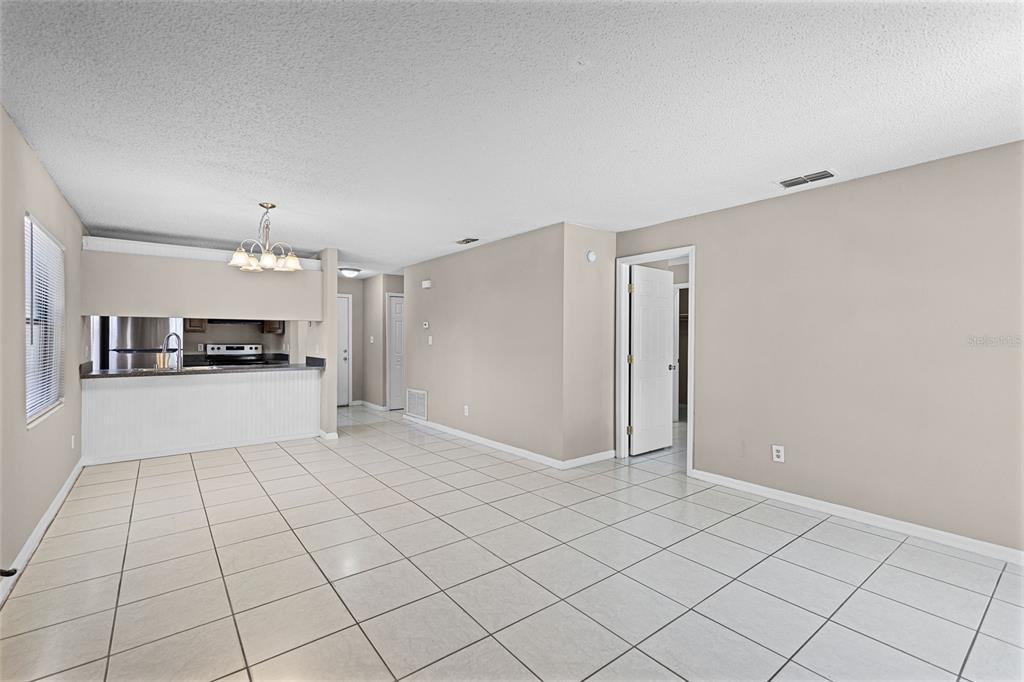 An open-concept room features white tile flooring, beige walls, and a kitchen pass-through window — 2530 KAMNIC COURT, WINTER PARK, FL