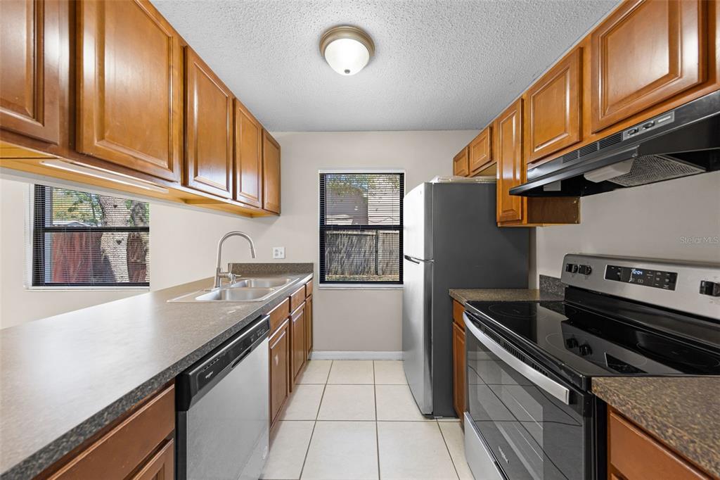 A kitchen features wood cabinets, stainless steel appliances, a double sink, and light-colored floor tiles — 2530 KAMNIC COURT, WINTER PARK, FL