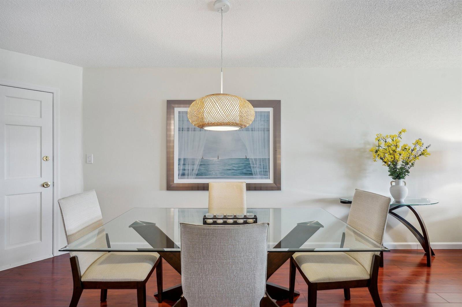 A dining room features a glass-topped table, upholstered chairs, a woven pendant light, and artwork — 5540 N Ocean Boulevard # 212, Ocean Ridge FL 33435, OCEAN RIDGE, FL