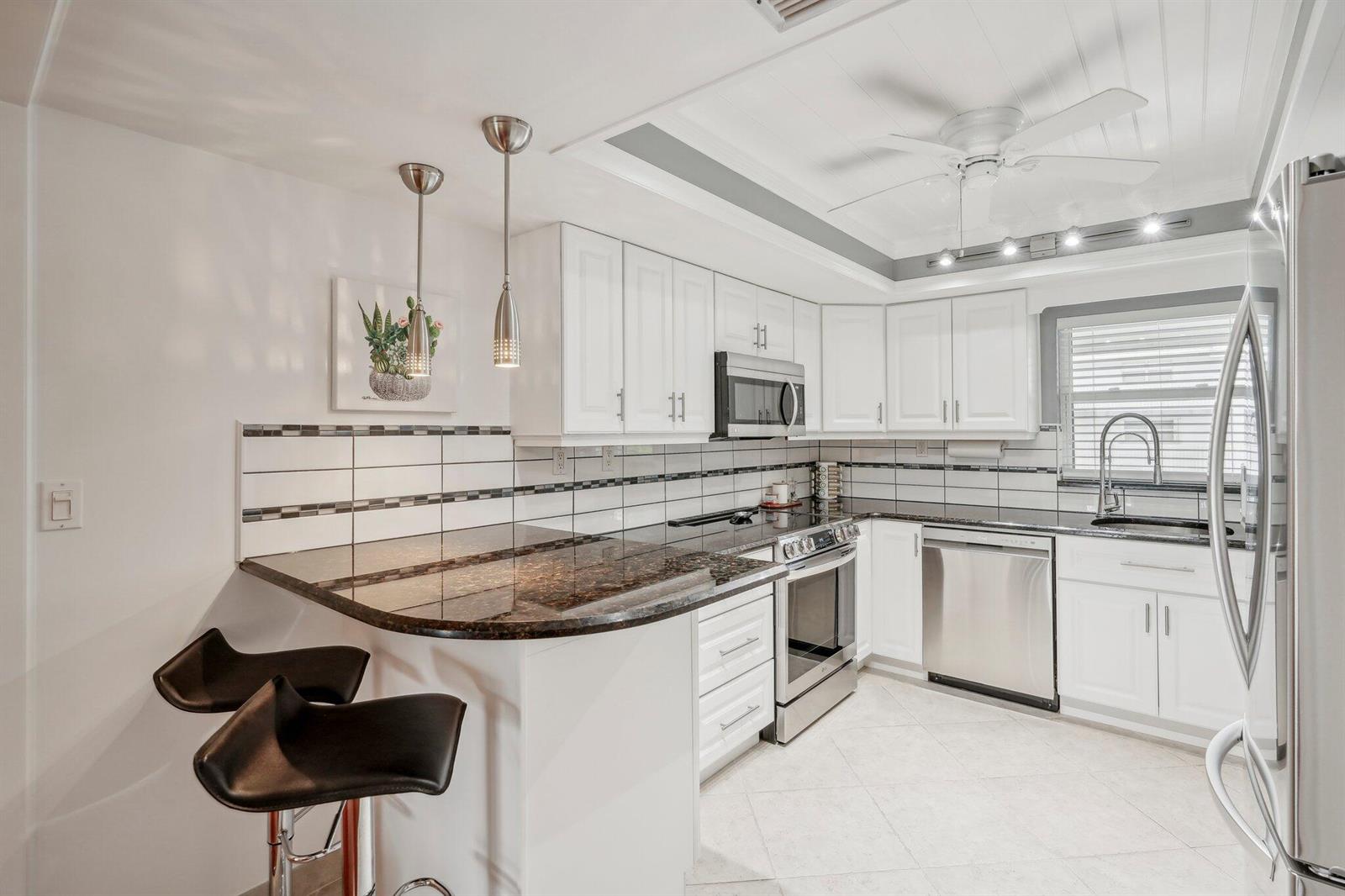 A kitchen with white cabinets, dark granite countertops, stainless steel appliances, and a breakfast bar — 5540 N Ocean Boulevard # 212, Ocean Ridge FL 33435, OCEAN RIDGE, FL