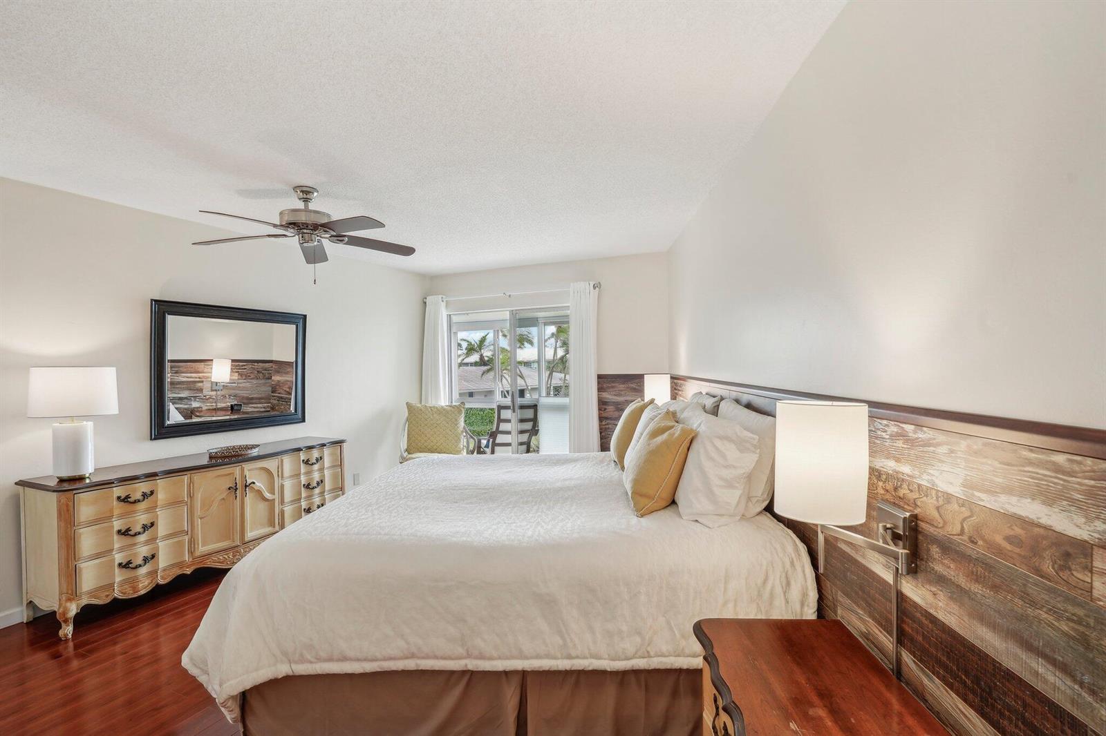 A bedroom features a king bed, wood-paneled accent wall, dresser, and a sliding glass door — 5540 N Ocean Boulevard # 212, Ocean Ridge FL 33435, OCEAN RIDGE, FL