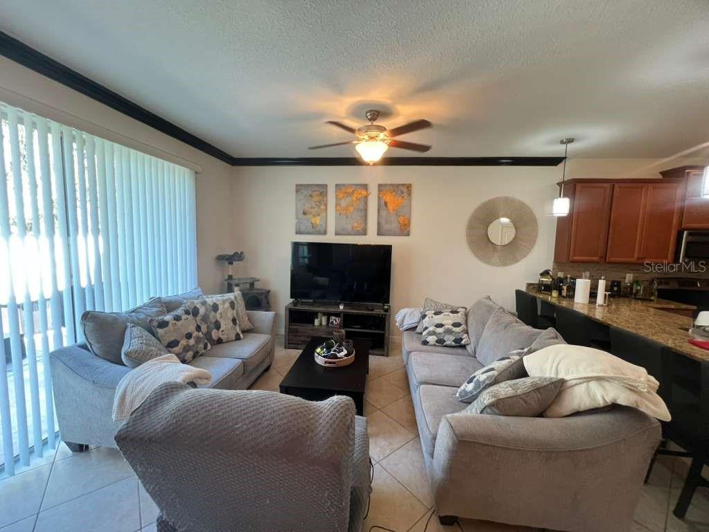 A living room features gray sofas, a television on a stand, and an open kitchen — 6453 SEDGEFORD DRIVE, LAKELAND, FL