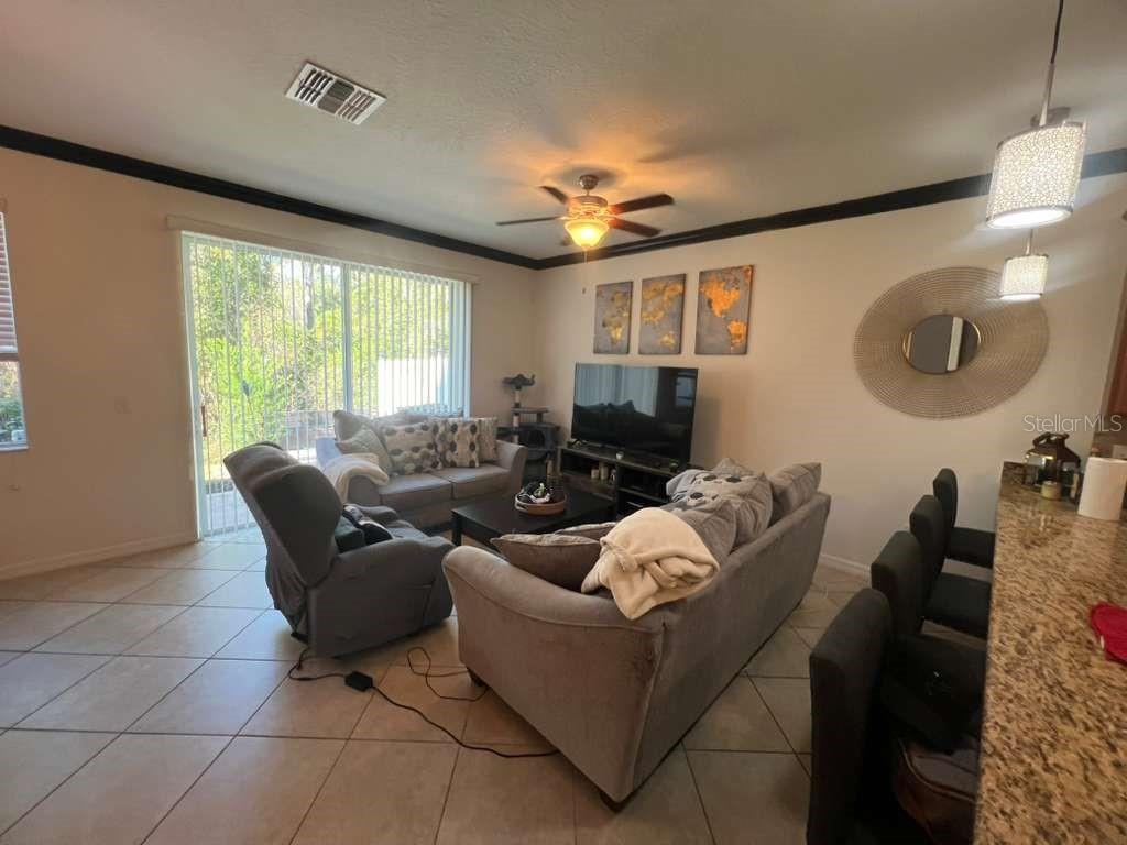A living room features tile flooring, a ceiling fan, a television, and gray furniture — 6453 SEDGEFORD DRIVE, LAKELAND, FL