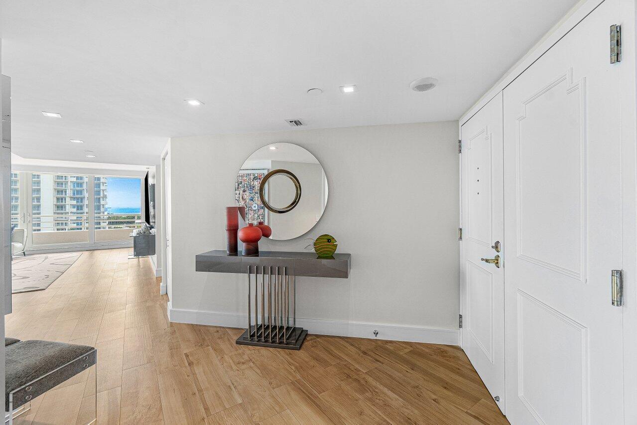 A modern entryway features light wood floors, a floating console table, and a circular mirror — 4201 N Ocean Boulevard # 601, Boca Raton FL 33431, BOCA RATON, FL