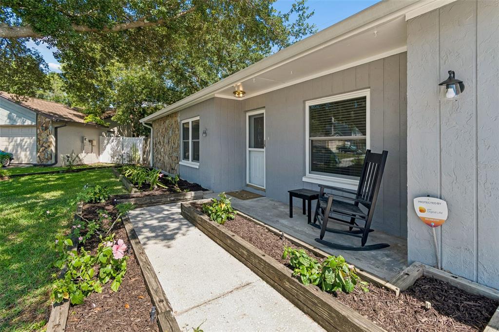 A gray house exterior features a concrete walkway, wooden planter beds, and a front porch — 16205 SAWGRASS CIRCLE, TAMPA, FL