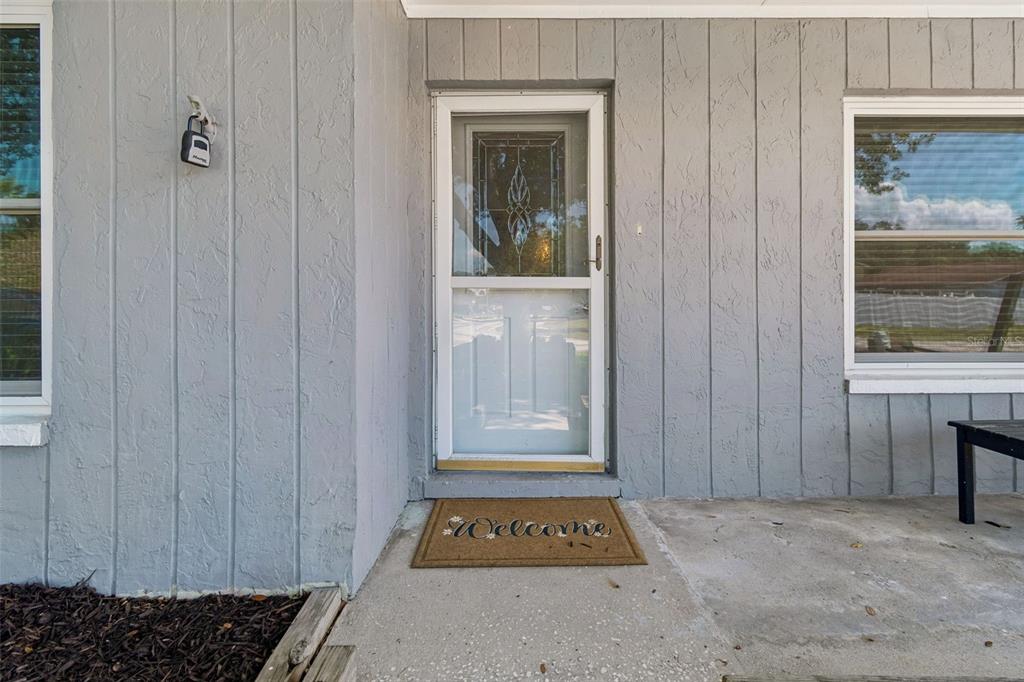 A gray house exterior features a front door with a storm door and a welcome mat — 16205 SAWGRASS CIRCLE, TAMPA, FL