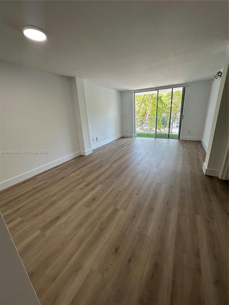 An empty room features light wood-look flooring, white walls, a ceiling light, and a sliding glass door — 777 NE 62nd St # C306, Miami FL 33138, MIAMI, FL