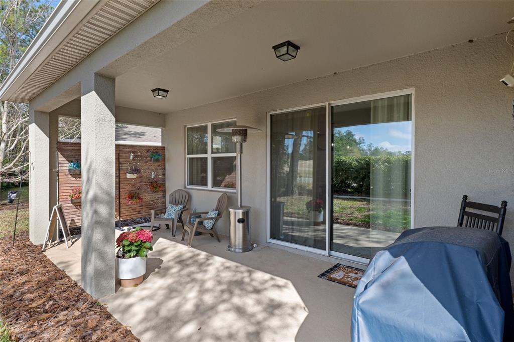 A covered concrete patio features a sliding glass door, outdoor seating, and a metal heater — 17807 GARSALASO CIRCLE, BROOKSVILLE, FL