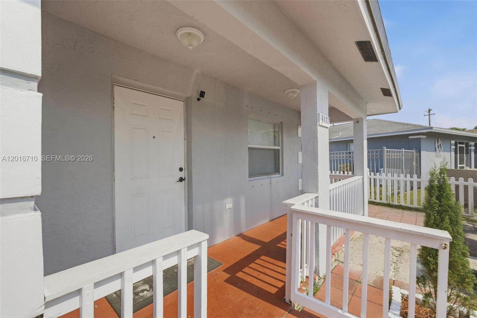 A white front door opens onto a covered porch with a red floor and railing — 3177 NW 75th Way, Hollywood FL 33024, HOLLYWOOD, FL