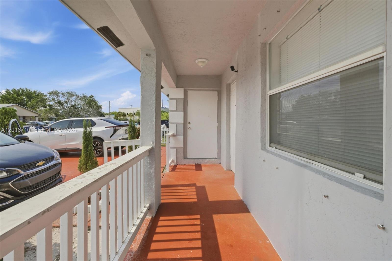 A covered outdoor porch features a white railing, orange flooring, and a white door — 3177 NW 75th Way, Hollywood FL 33024, HOLLYWOOD, FL