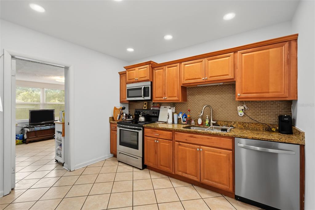 A kitchen with wood cabinets, granite countertops, stainless steel appliances, and beige tile flooring — 1542 LAKEVIEW ROAD, CLEARWATER, FL