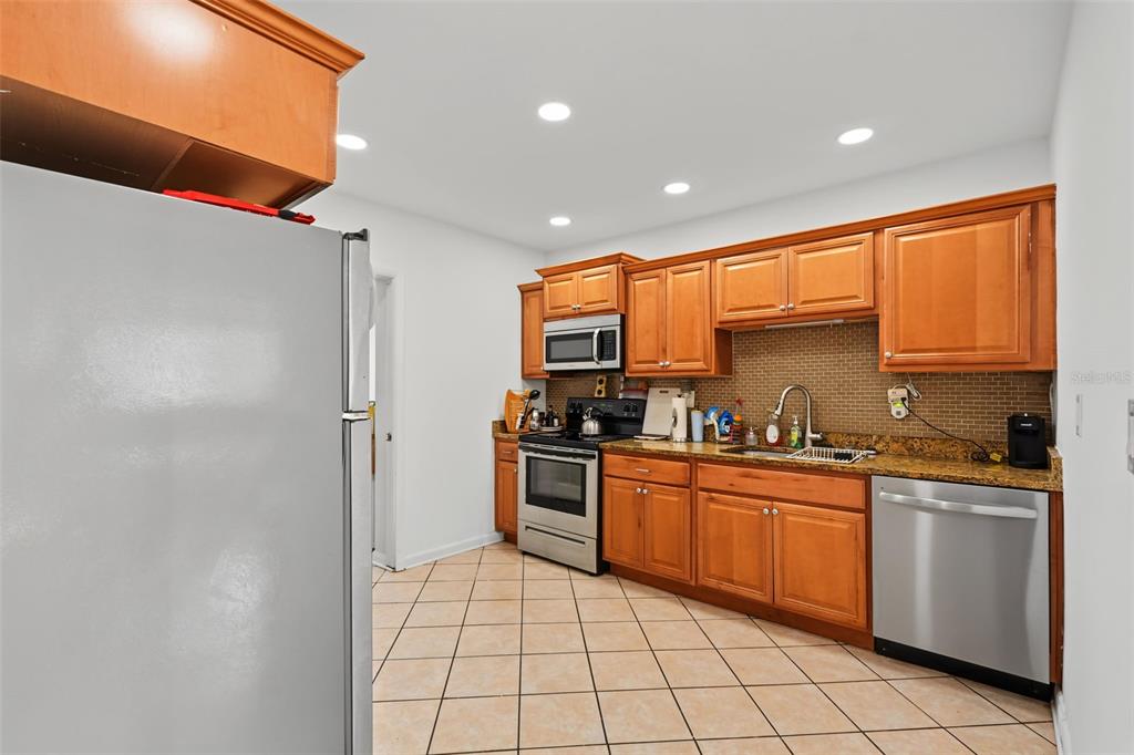 A kitchen features wood cabinets, granite countertops, stainless steel appliances, and beige tile flooring — 1542 LAKEVIEW ROAD, CLEARWATER, FL