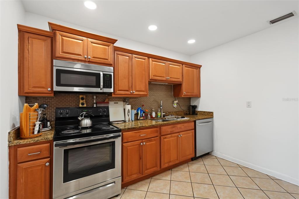 A kitchen features wood cabinets, granite countertops, stainless steel appliances, and tiled flooring — 1542 LAKEVIEW ROAD, CLEARWATER, FL