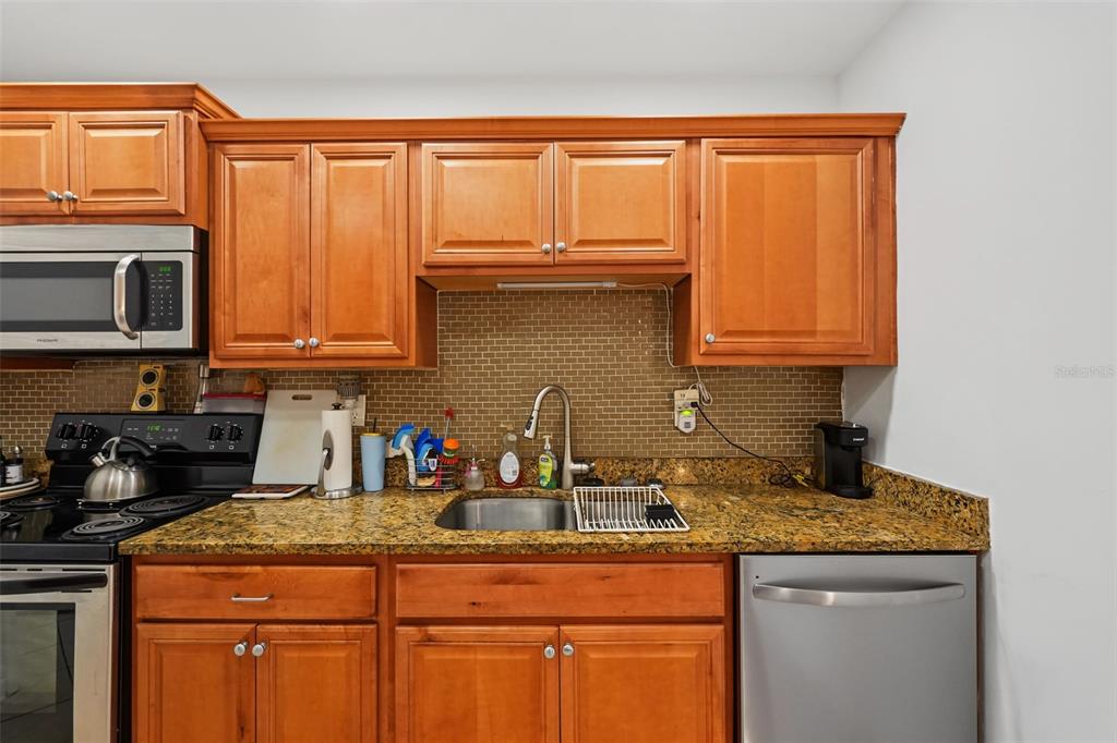 A kitchen features wood cabinets, granite countertops, a stainless steel sink, and a tiled backsplash — 1542 LAKEVIEW ROAD, CLEARWATER, FL
