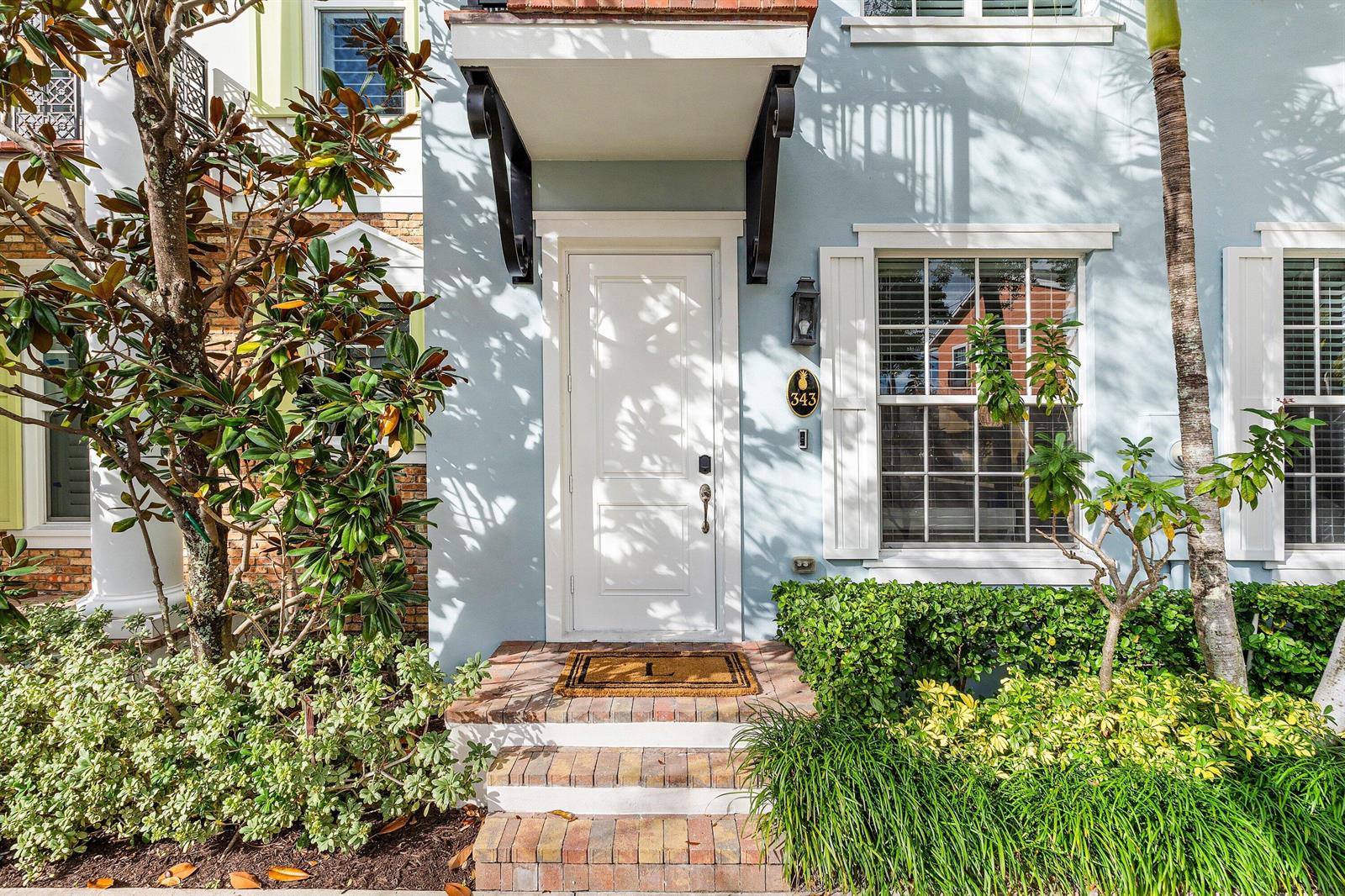 The exterior of a light blue house features a white front door and brick steps — 343 E Cannery Row Circle, Delray Beach FL 33444, DELRAY BEACH, FL