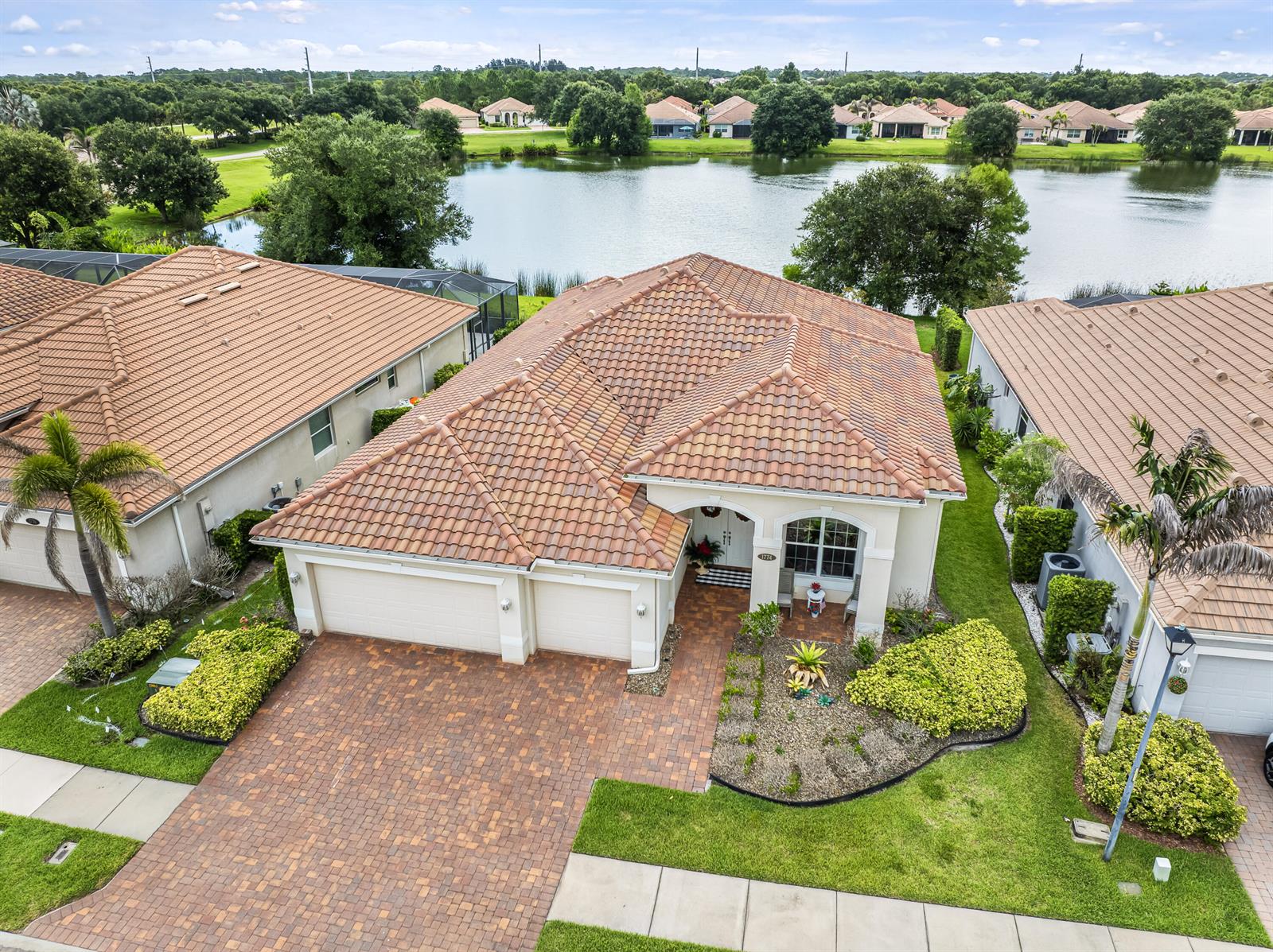 An aerial view shows a house with a tiled roof, paver driveway, and lakefront backyard — 1774 Belmont Circle SW, Vero Beach FL 32968, VERO BEACH, FL