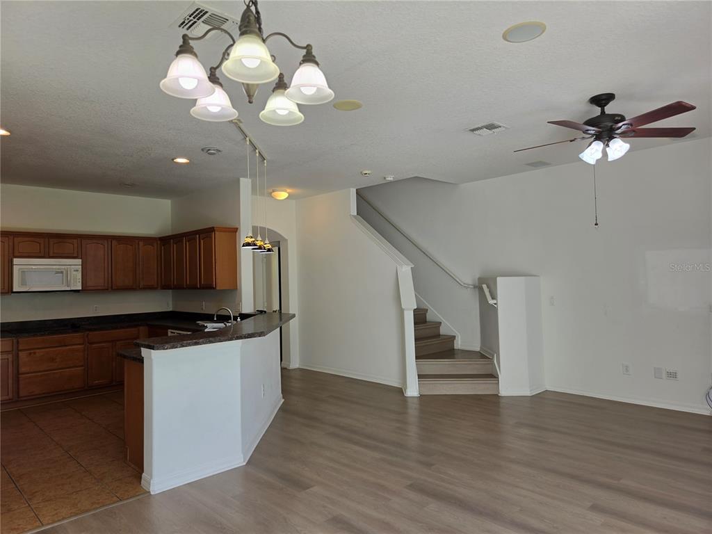 A kitchen with wood cabinets and a breakfast bar opens to a living area with stairs — 3659 SOARING LANE, SANFORD, FL