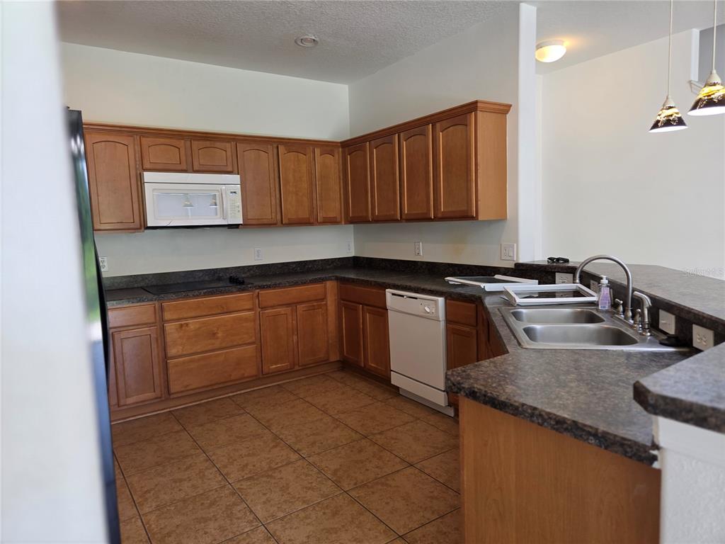 A kitchen features wood cabinets, dark laminate countertops, tile flooring, and white appliances — 3659 SOARING LANE, SANFORD, FL