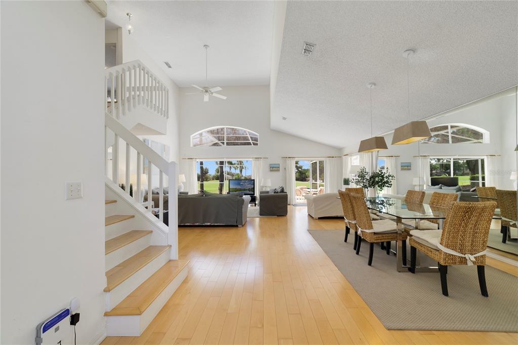 A bright, open-concept living and dining area features light wood flooring, vaulted ceilings, and stairs — 2135 MALLORY CIRCLE, HAINES CITY, FL