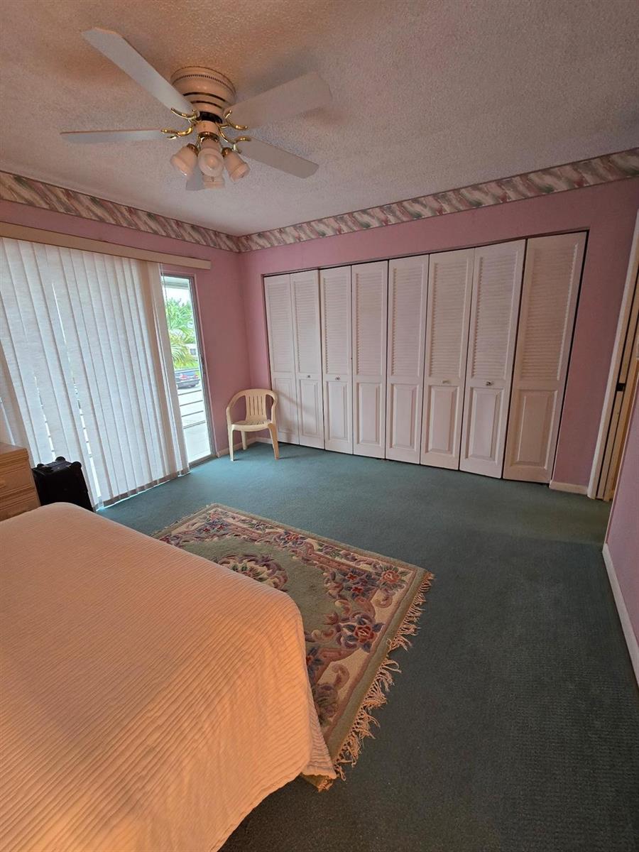 A bedroom features pink walls, green carpeting, a ceiling fan, and a wall of closets — 456 Tilford U # 456, Deerfield Beach FL 33442, DEERFIELD BEACH, FL
