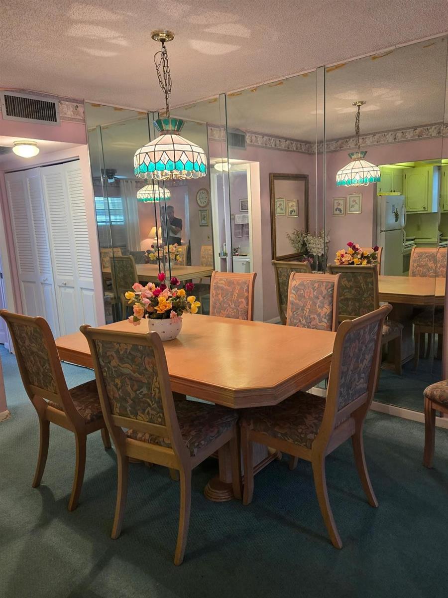 A dining room features a wooden table, patterned chairs, a stained-glass pendant light, and mirrored walls — 456 Tilford U # 456, Deerfield Beach FL 33442, DEERFIELD BEACH, FL
