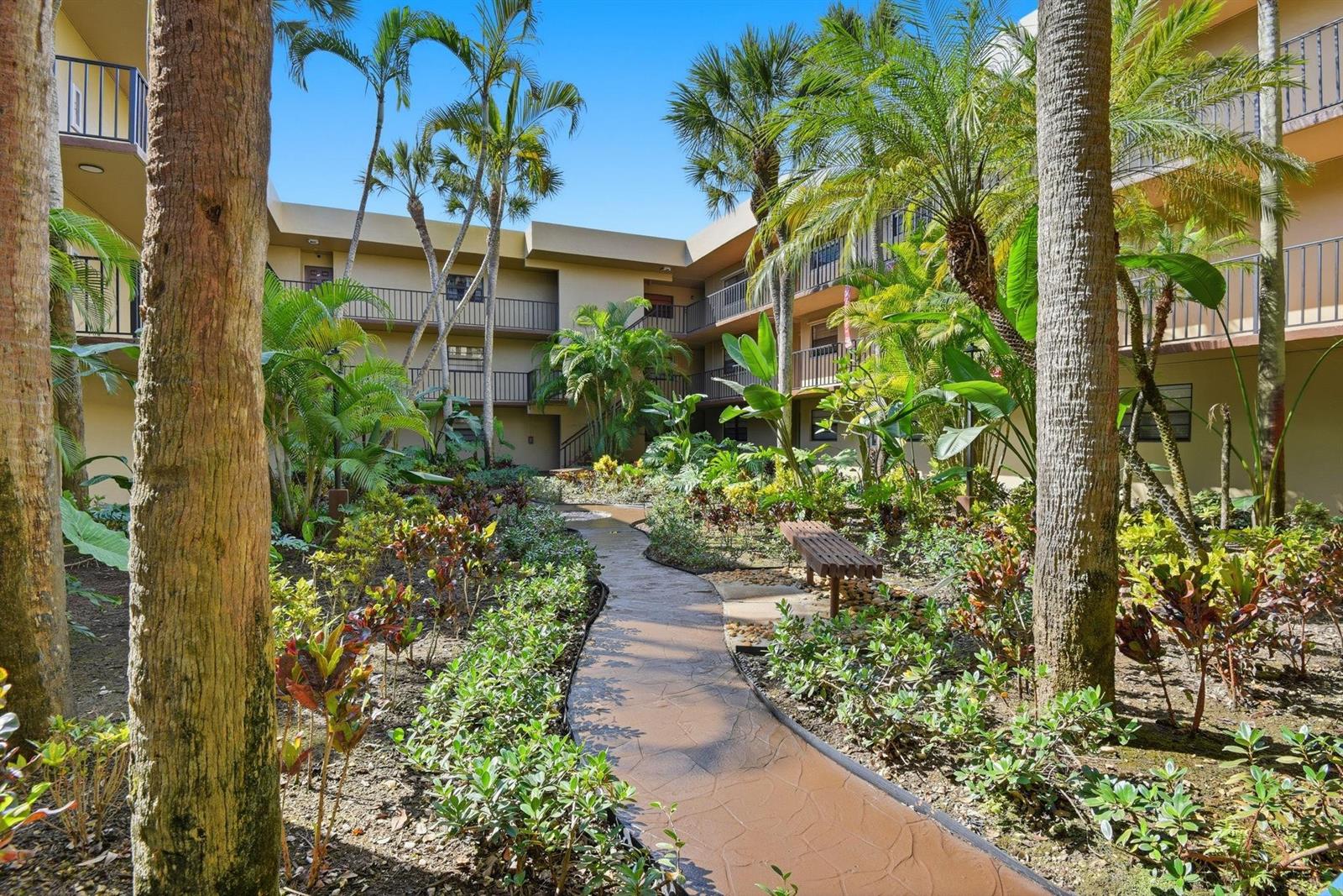 A landscaped courtyard with a winding stone path, tropical plants, and a multi-story apartment building — 10875 SW 112th Avenue # 202, Miami FL 33176, MIAMI, FL