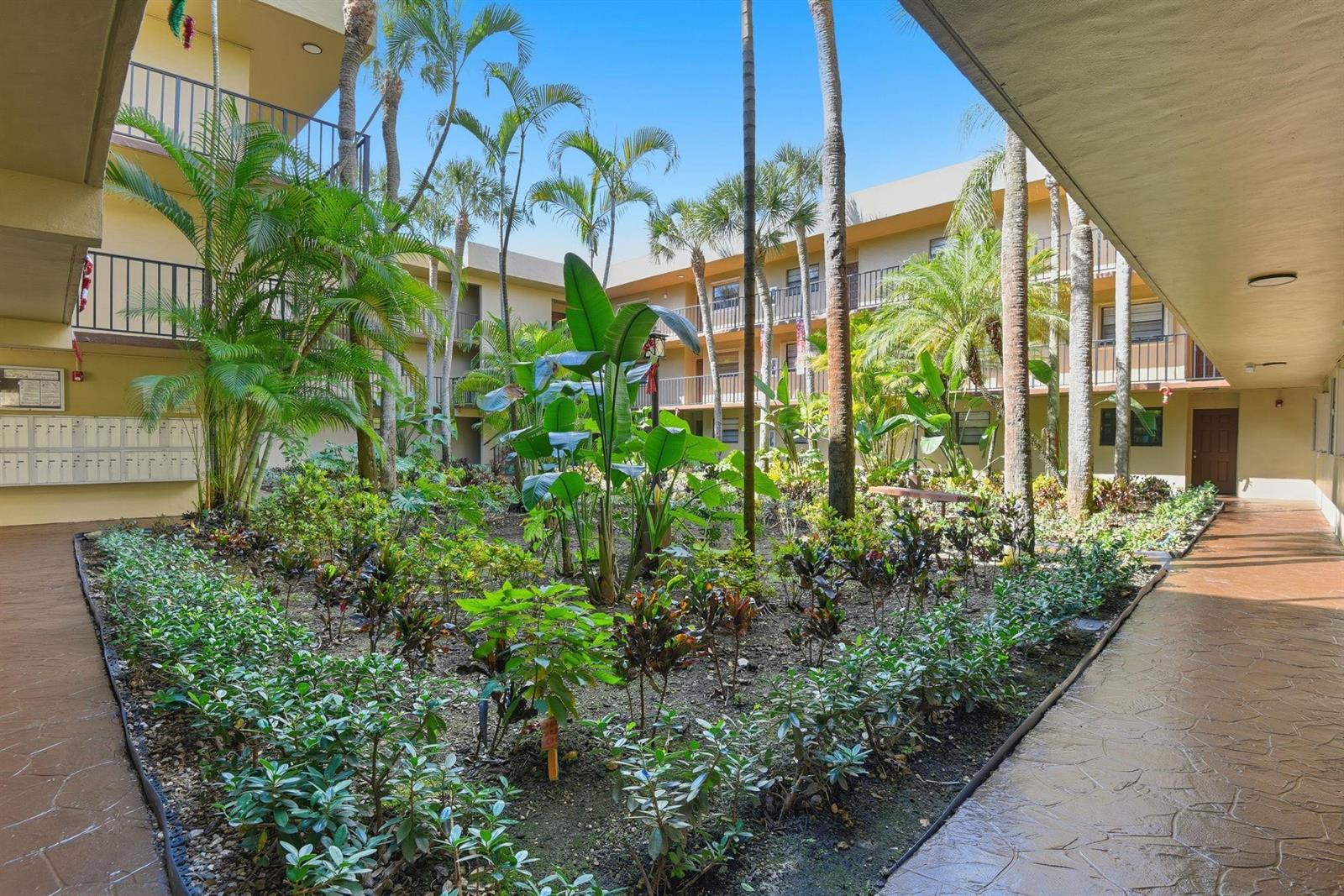An open-air courtyard with lush tropical landscaping surrounded by a multi-story apartment building — 10875 SW 112th Avenue # 202, Miami FL 33176, MIAMI, FL