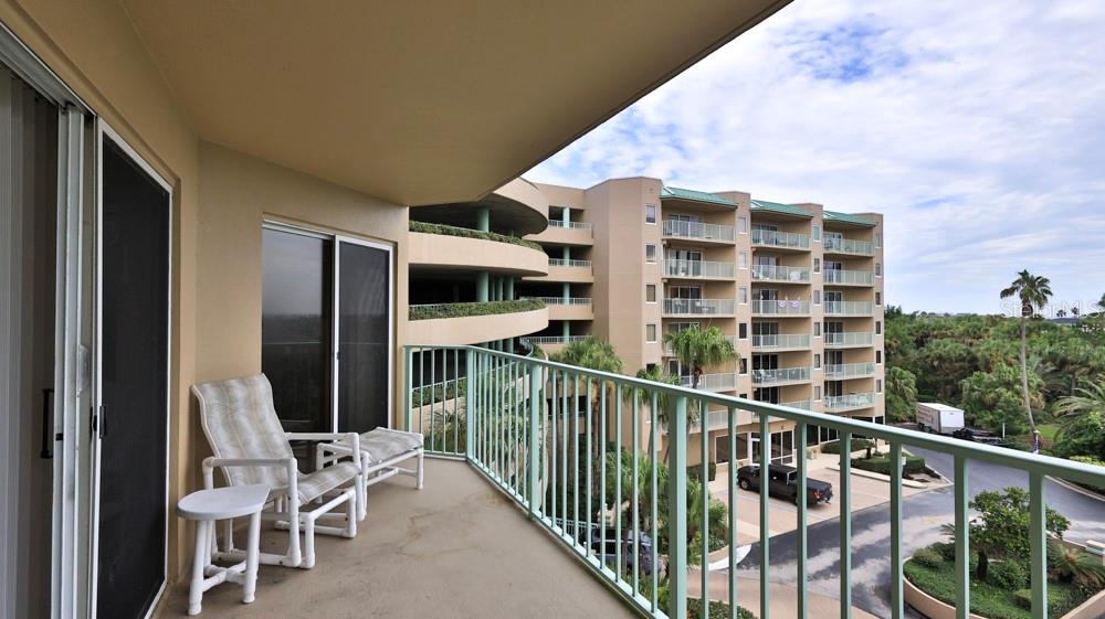 A balcony with white patio furniture overlooks a parking area and a multi-story apartment building — 4 OCEANS WEST BOULEVARD UNIT 508D, DAYTONA BEACH SHORES, FL